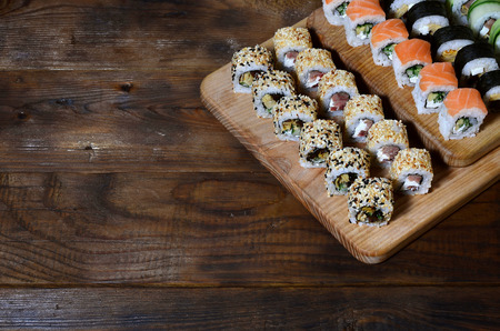Sushi set of a number of rolls is located on a wooden cutting board on a table in the kitchen of a sushi bar. A traditional dish of oriental cuisineの写真素材