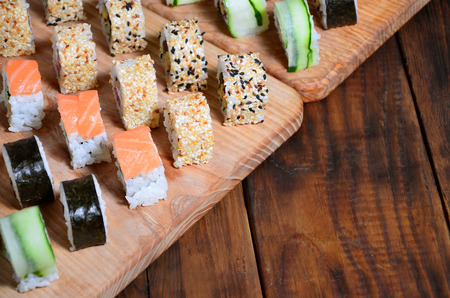 Sushi set of a number of rolls is located on a wooden cutting board on a table in the kitchen of a sushi bar. A traditional dish of oriental cuisineの写真素材