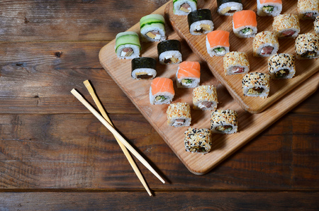 A detailed shot of a set of Japanese sushi rolls and a device for their use (chopsticks), which are located on a wooden cutting board on a table in the kitchen of a sushi barの写真素材
