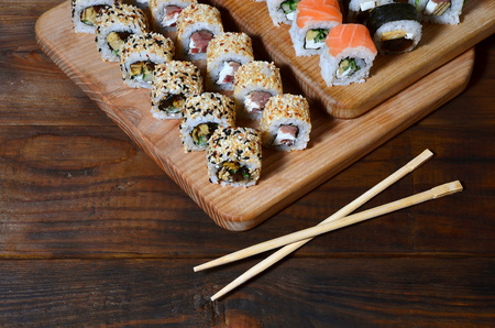 A detailed shot of a set of Japanese sushi rolls and a device for their use (chopsticks), which are located on a wooden cutting board on a table in the kitchen of a sushi barの写真素材