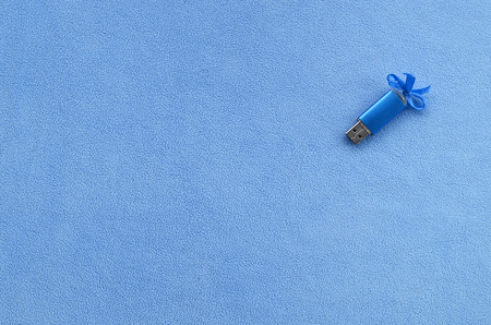 Brilliant blue usb flash memory card with a blue bow lies on a blanket of soft and furry light blue fleece fabric. Classic female gift design for a memory cardの写真素材