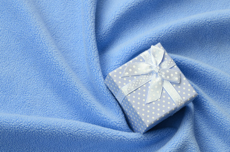 A small gift box in blue with a small bow lies on a blanket of soft and furry light blue fleece fabric with a lot of relief folds. Packing for a gift to your lovely girlfriendの写真素材