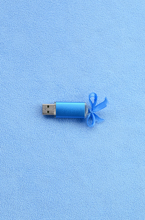 Brilliant blue usb flash memory card with a blue bow lies on a blanket of soft and furry light blue fleece fabric. Classic female gift design for a memory cardの写真素材