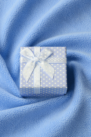 A small gift box in blue with a small bow lies on a blanket of soft and furry light blue fleece fabric with a lot of relief folds. Packing for a gift to your lovely girlfriendの写真素材