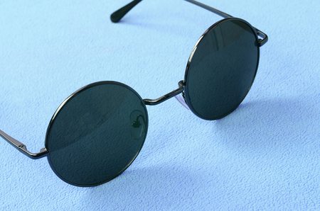 Stylish black sunglasses with round glasses lies on a blanket made of soft and fluffy light blue fleece fabric. Fashionable background picture in female colorsの写真素材