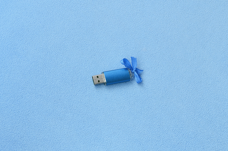 Brilliant blue usb flash memory card with a blue bow lies on a blanket of soft and furry light blue fleece fabric. Classic female gift design for a memory cardの写真素材
