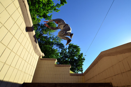 A young guy performs a jump through the space between the concrete parapets. The athlete practices parkour, training in street conditions. Bottom viewの写真素材