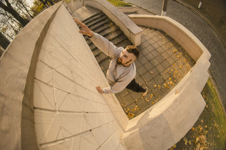 A young guy overcomes obstacles, climbing on concrete walls. The athlete practices parkour, training in street conditions. The concept of sports subcultures among youthの写真素材