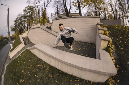 A young guy performs a jump through the concrete parapet. The athlete practices parkour, training in...
