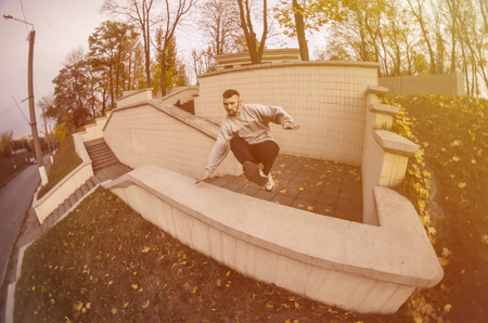 A young guy performs a jump through the concrete parapet. The athlete practices parkour, training in street conditions. The concept of sports subcultures among youthの写真素材