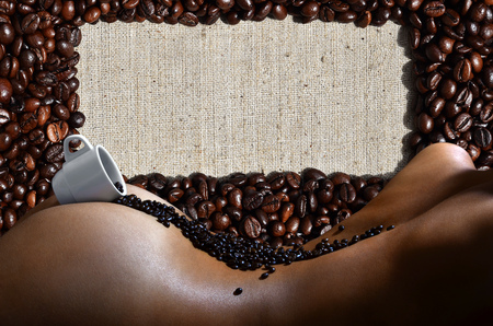 A photograph of a white cup of hot coffee with lots of coffee beans, which lies on a beautiful and sexy naked female body with a many beans in background pattern. Erotic photo about the coffee drinksの写真素材