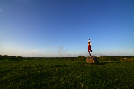 Silhouette of young blonde girl in sport suit practice yoga on a picturesque green hill in the evening at sunset. The concept of exercising and healthy lifestylesの写真素材
