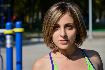 Portrait of a young caucasian athlete girl in a bright green sportswear against the backdrop of a street sports gym for outdoor athletics training. Summer sports in the open airの写真素材
