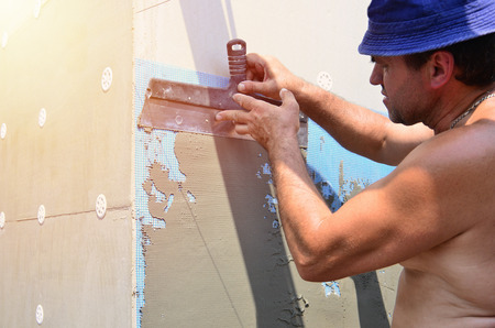 Fifty years old manual worker with wall plastering tools renovating house. Plasterer renovating walls and corners with spatula and plaster. Wall mash installation. Construction finishing worksの写真素材