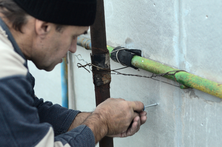 An elderly worker creates holes in the expanded polystyrene wall for the subsequent drilling and installation of an umbrella dowel. The process of fixing expanded polystyrene plates. Insulation workの写真素材
