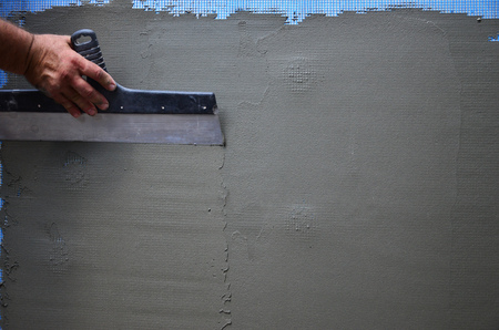 Hands of an old manual worker with wall plastering tools renovating house. Plasterer renovating...