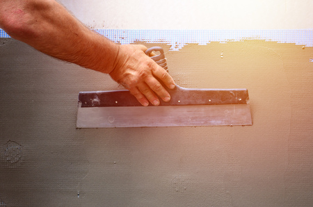 Hands of an old manual worker with wall plastering tools renovating house. Plasterer renovating...