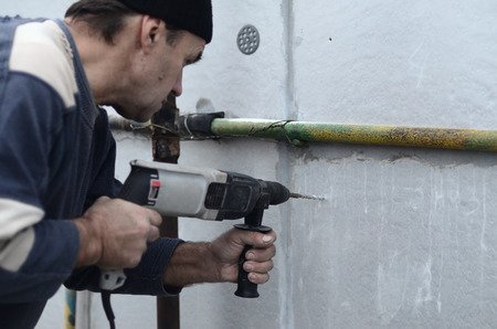 An elderly workman drills a hole in a styrofoam wall for the subsequent installation of a plastic reinforcing dowel. Creating holes in the wall with a drill. Warming of the building facadeの写真素材