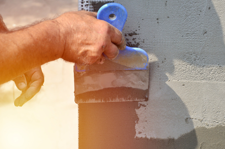 Hands of an old manual worker with wall plastering tools renovating house. Plasterer renovating outdoor walls and corners with spatula and plaster. Wall insulation. Construction finishing worksの写真素材