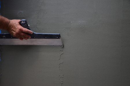 Hands of an old manual worker with wall plastering tools renovating house. Plasterer renovating outdoor walls and corners with spatula and plaster. Wall insulation. Construction finishing worksの写真素材