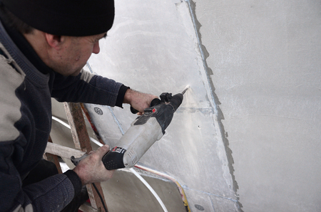 An elderly workman drills a hole in a styrofoam wall for the subsequent installation of a plastic reinforcing dowel. Creating holes in the wall with a drill. Warming of the building facadeの写真素材