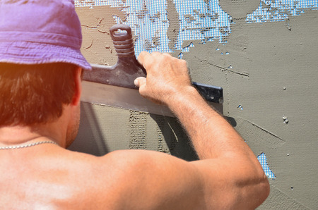 Fifty years old manual worker with wall plastering tools renovating house. Plasterer renovating walls and corners with spatula and plaster. Wall mash installation. Construction finishing worksの写真素材