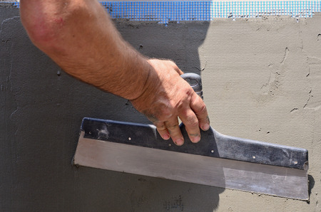 Hands of an old manual worker with wall plastering tools renovating house. Plasterer renovating outdoor walls and corners with spatula and plaster. Wall insulation. Construction finishing worksの写真素材