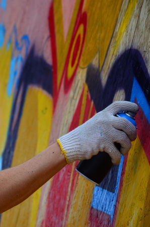 A hand with a spray can that draws a new graffiti on the wall. Photo of the process of drawing a graffiti on a wooden wall close-up. The concept of street art and illegal vandalismの写真素材