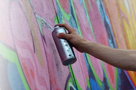 A young red-haired graffiti artist paints a new graffiti on the wall. Photo of the process of drawing a graffiti on a wall close-up. The concept of street art and illegal vandalismの写真素材