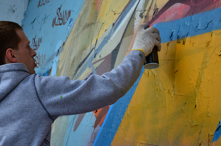 A young red-haired graffiti artist paints a new graffiti on the wall. Photo of the process of drawing a graffiti on a wall close-up. The concept of street art and illegal vandalismの写真素材