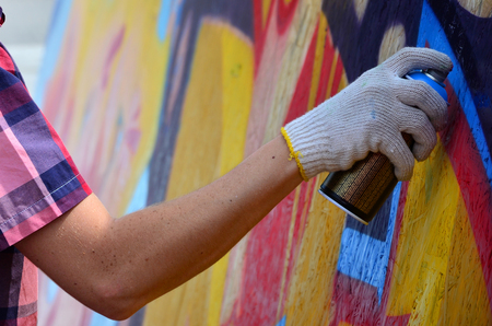 A hand with a spray can that draws a new graffiti on the wall. Photo of the process of drawing a graffiti on a wooden wall close-up. The concept of street art and illegal vandalismの写真素材