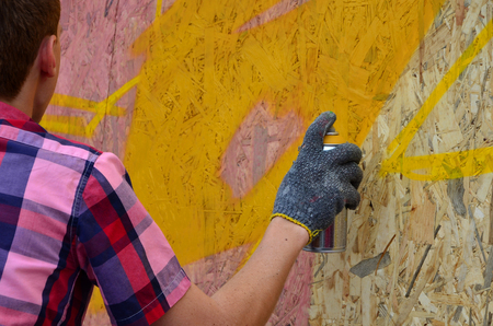 A young red-haired graffiti artist paints a new graffiti on the wall. Photo of the process of drawing a graffiti on a wall close-up. The concept of street art and illegal vandalismの写真素材