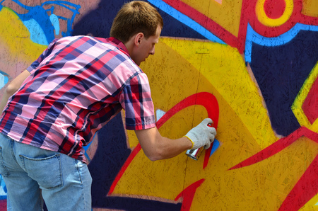 A young red-haired graffiti artist paints a new graffiti on the wall. Photo of the process of drawing a graffiti on a wall close-up. The concept of street art and illegal vandalismの写真素材