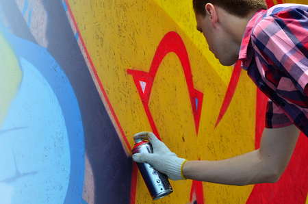 A young red-haired graffiti artist paints a new graffiti on the wall. Photo of the process of drawing a graffiti on a wall close-up. The concept of street art and illegal vandalismの写真素材
