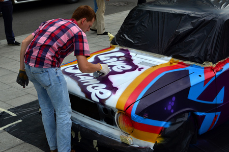 A young red-haired graffiti artist paints a new colorful graffiti on the car. Photo of the process of drawing a graffiti on a car close-up. The concept of street art and illegal vandalismの写真素材