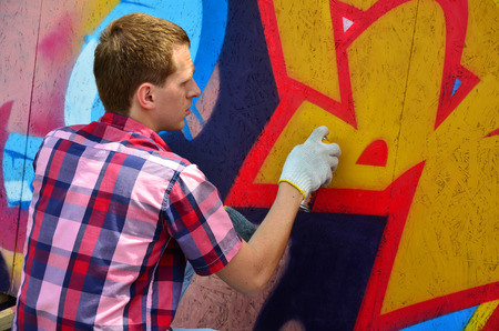 A young red-haired graffiti artist paints a new graffiti on the wall. Photo of the process of drawing a graffiti on a wall close-up. The concept of street art and illegal vandalismの写真素材
