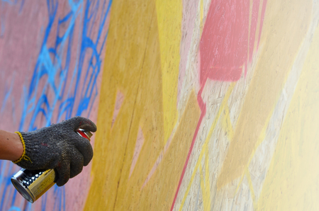 A hand with a spray can that draws a new graffiti on the wall. Photo of the process of drawing a graffiti on a wooden wall close-up. The concept of street art and illegal vandalismの写真素材