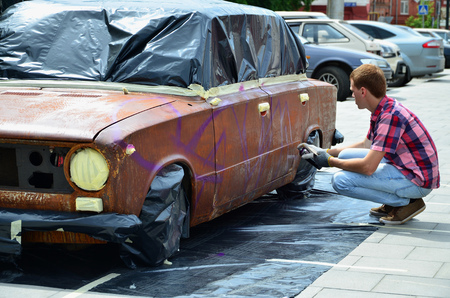 A young red-haired graffiti artist paints a new colorful graffiti on the car. Photo of the process of drawing a graffiti on a car close-up. The concept of street art and illegal vandalismの写真素材