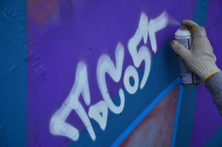 A hand with a spray can that draws a new graffiti on the wall. Photo of the process of drawing a graffiti on a concrete wall close-up. The concept of street art and illegal vandalismの写真素材
