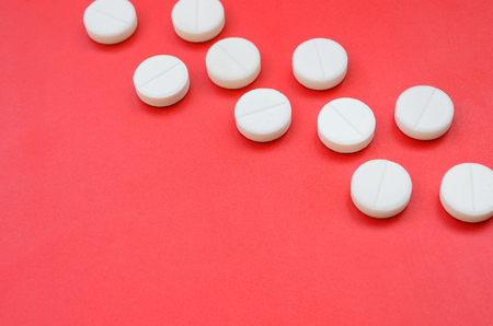 A few white tablets lie on a bright red background surface. Background image on medical and pharmaceutical topicsの写真素材