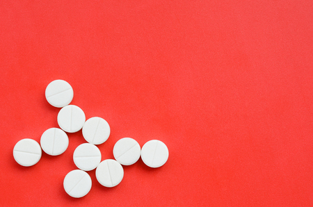 Several white tablets lie on a bright red background in the form of a bacterium. Background image on medicine and pharmaceutical topicsの写真素材