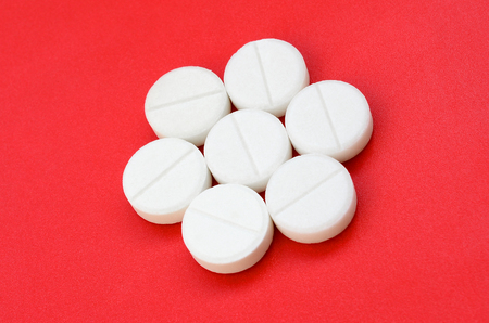 A few white tablets lie on a bright red background surface. Background image on medical and pharmaceutical topicsの写真素材