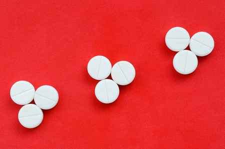 Several white tablets lie on a bright red background in the form of three triangular arrows. Background image on medicine and pharmaceutical topicsの写真素材
