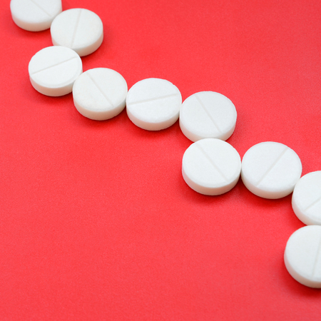 A few white tablets lie on a bright red background surface. Background image on medical and pharmaceutical topicsの写真素材