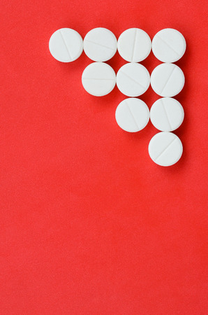Several white tablets lie on a bright red background in the form of a triangular arrow. Background image on medicine and pharmaceutical topicsの写真素材