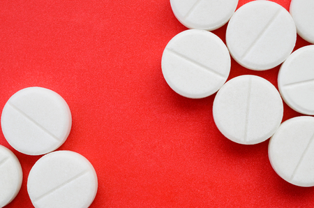 A few white tablets lie on a bright red background surface. Background image on medical and pharmaceutical topicsの写真素材