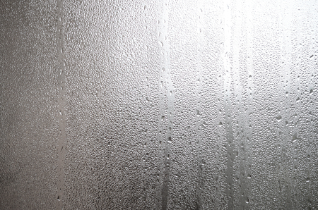 A photo of the glass surface of the window, covered with a multitude of droplets of various sizes. Background texture of a dense layer of condensate on glassの写真素材