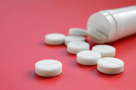 Several white tablets fall out of the plastic jar on the red surface. Background image on medical and pharmaceutical topicsの写真素材