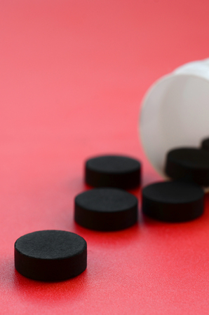 Several black tablets fall out of the plastic jar on the red surface. Background image on medical and pharmaceutical topics. Activated Charcoalの写真素材