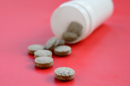 Several brown tablets fall out of the plastic jar on the red surface. Background image on medical and pharmaceutical topicsの写真素材